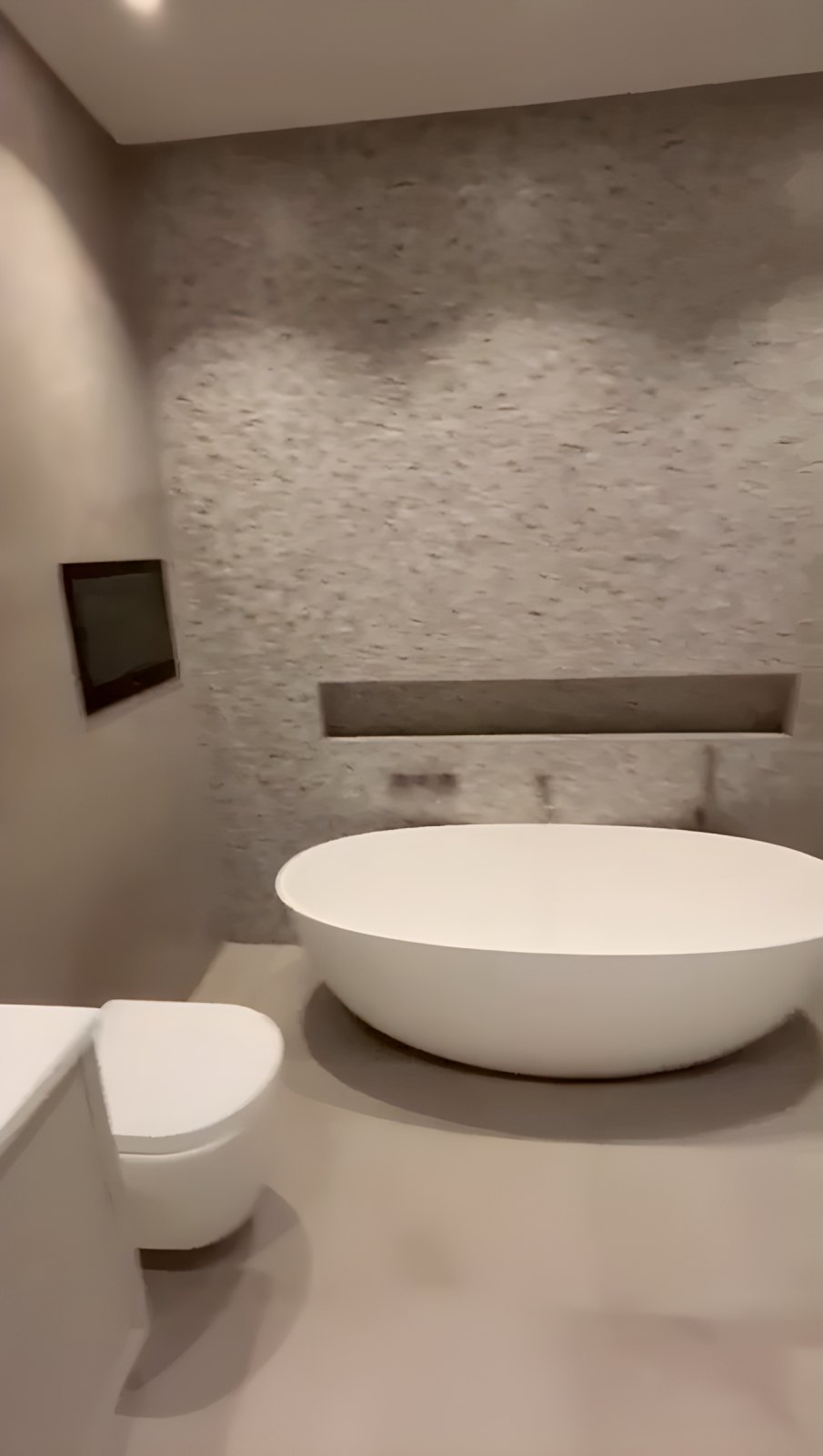 Bathroom with a freestanding bath, textured stone feature wall and wall-hung WC