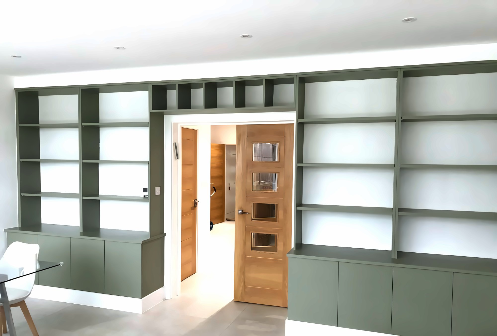 Sage green fitted shelving and cupboards built around a doorway