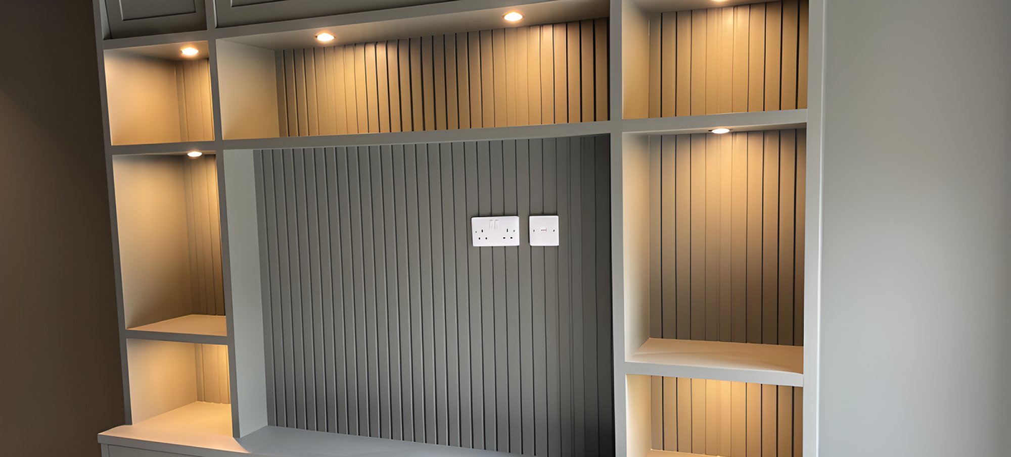 Sage green fitted TV unit with fluted panelling, lit shelves and cupboards below