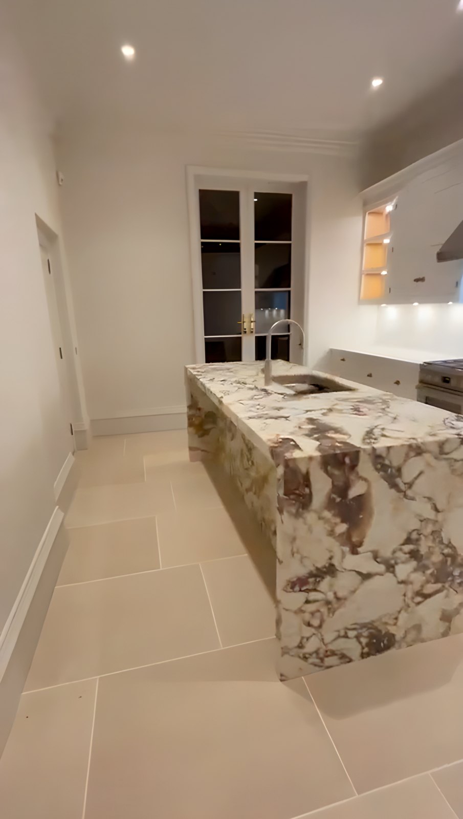Kitchen with a marble waterfall island, painted units and stone floor tiles